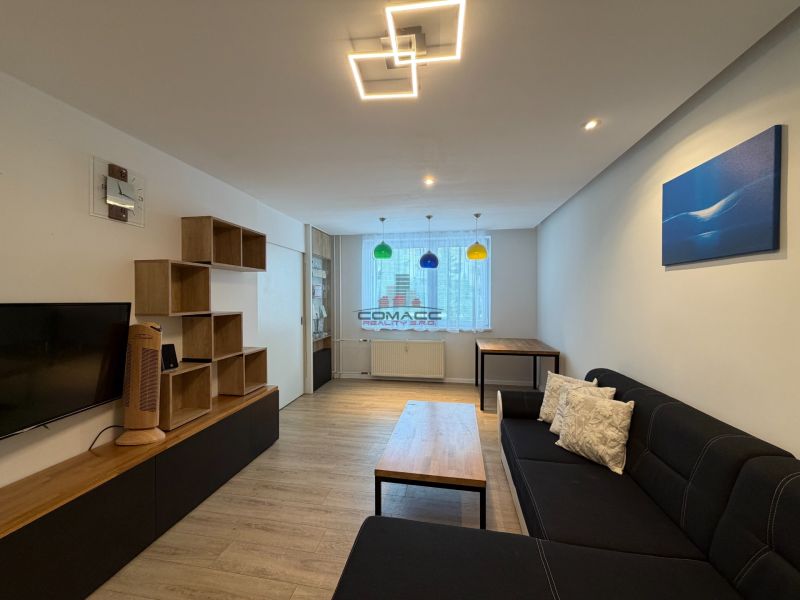Wohnzimmer in einer 3-Zimmer-Wohnung mit Holzboden und schwarzem Sofa.