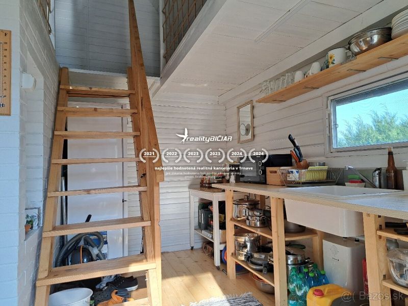 Innenraum einer Hütte mit Treppe, Küche und Boden in Holzoptik.