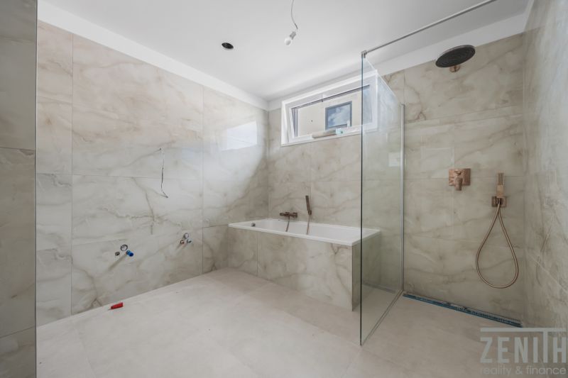 Ein Badezimmer in einem Einfamilienhaus mit Badewanne und Dusche, gefliest mit hellen Fliesen.