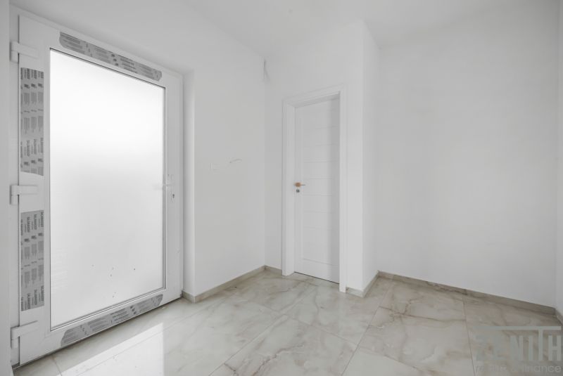 Weißer Eingangsbereich im Einfamilienhaus mit Fliesen und Türen.