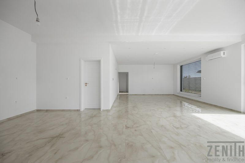 Ein geräumiges Zimmer mit einem großen Fenster und einem Boden in Holzoptik in einem Einfamilienhaus.