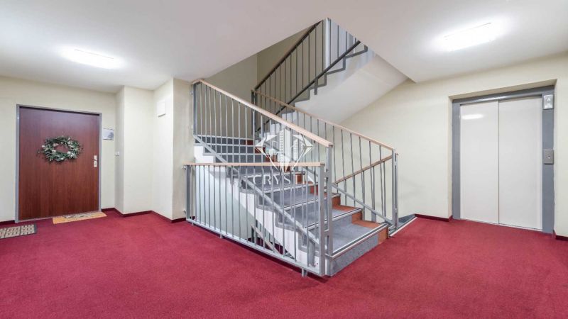 Flur in einem Ferienapartment mit rotem Teppich, Treppe und Aufzug.