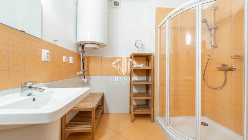 Badezimmer mit orangefarbenen Fliesen, Duschkabine und Waschbecken in einer Ferienwohnung.