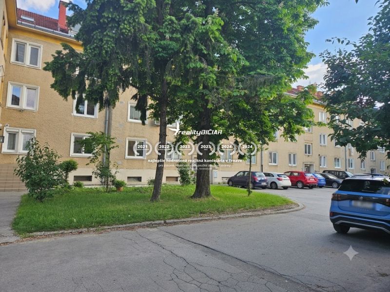 Parkplatz bei den 3-Zimmer-Wohnungen in der Študentská-Straße in Trnava, umgeben von Grünflächen und Bäumen.