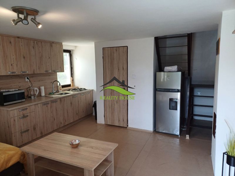 Innenraum einer Hütte mit Küchenzeile, Kühlschrank und Treppe, Boden mit Holzdekor.
