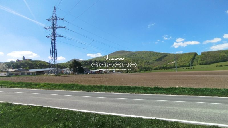 Landschaft an der Továrenská in Smolenice mit landwirtschaftlichen und forstwirtschaftlichen Flächen und Stromleitungen.