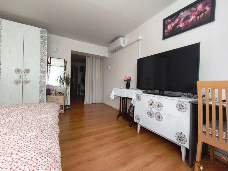 Schlafzimmer mit Holzboden, Fernseher, Schrank und Blumendekoration.