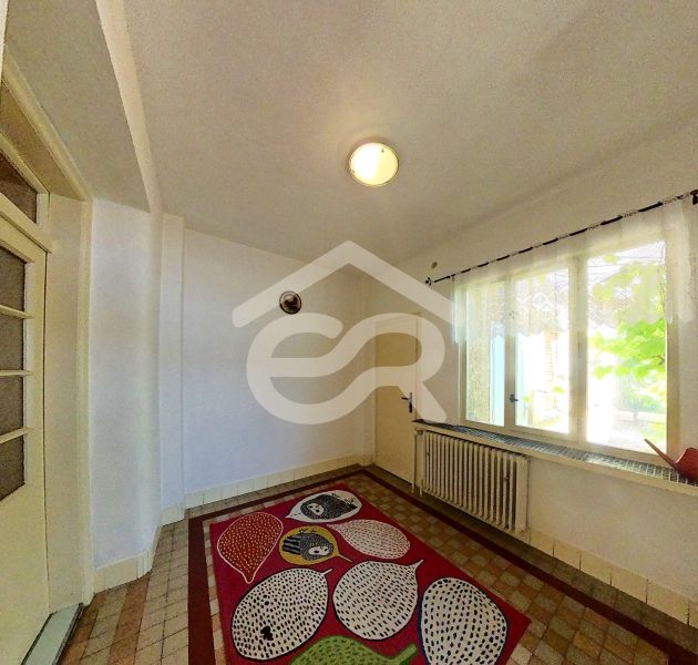 In einem Einfamilienhaus gibt es ein Zimmer mit einem bunten Teppich, einem Fenster und einer Wand mit einem Heizkörper.