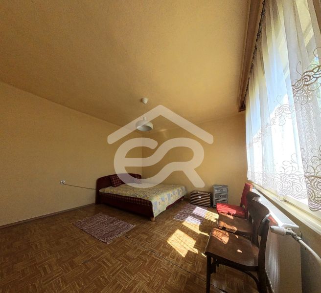 Helles Zimmer im Einfamilienhaus mit Bett, großem Fenster und Boden in Holzoptik.