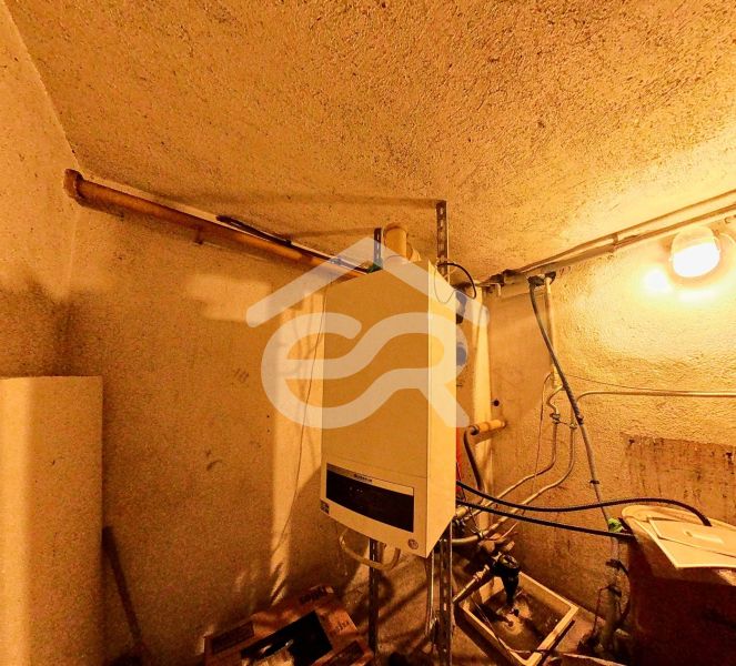 Badezimmer in einem Einfamilienhaus mit Einrichtung und Rohrleitungen, beleuchtet von einer Glühbirne.