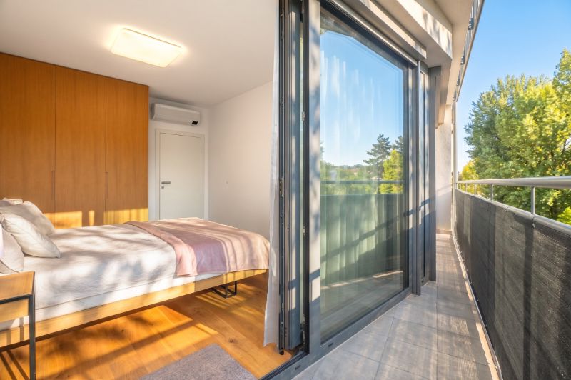 Schlafzimmer mit großer Glaswand, Holzboden und Balkon in einer Zweizimmerwohnung.