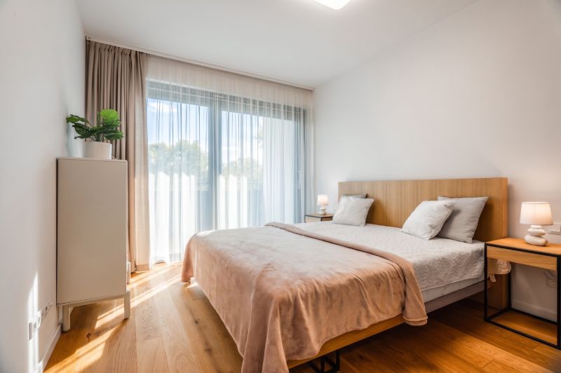 Schlafzimmer in einer 2-Zimmer-Wohnung mit Bett, Vorhängen, Nachttischen und einem Boden mit Holzdekor.