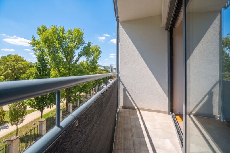Balkon einer 2-Zimmer-Wohnung mit Blick auf Grünflächen und blauen Himmel.
