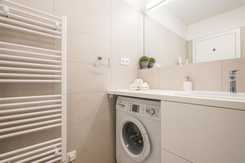 Badezimmer mit hellen Fliesen, Waschmaschine, Waschbecken und Handtüchern in einer 2-Zimmer-Wohnung.