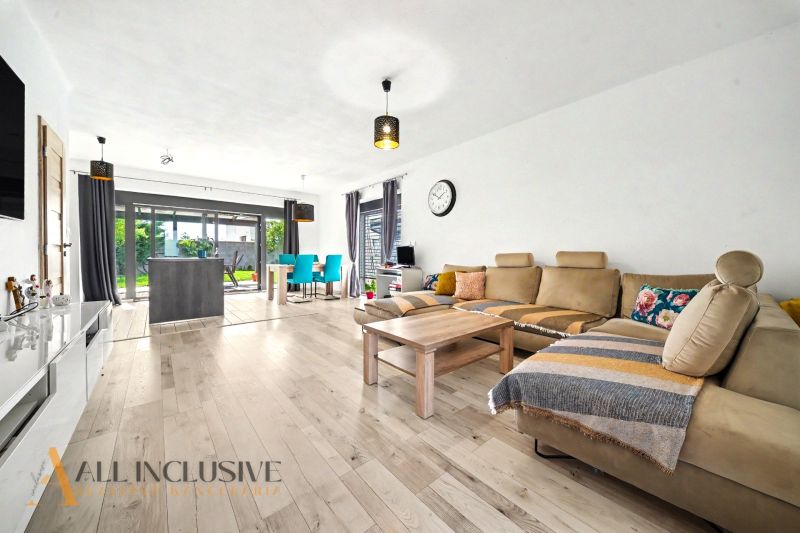Wohnzimmer in einem Einfamilienhaus mit Holzboden und großen Fenstern zum Garten.