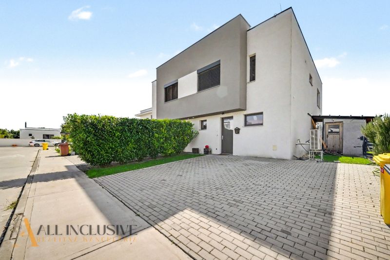 Ein Einfamilienhaus in Hrubá Borša mit gepflastertem Parkplatz und gepflegtem Grünbereich.