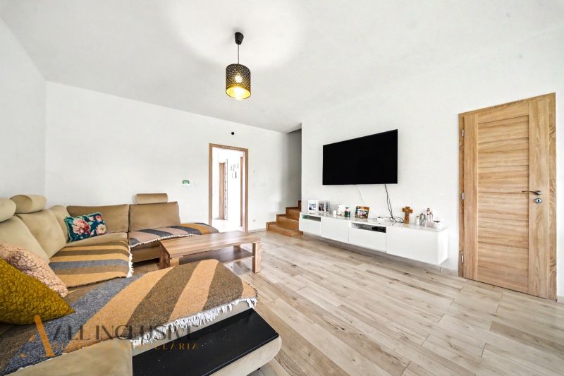 Wohnzimmer in einem Einfamilienhaus mit beigem Sofa und Boden in Holzoptik.