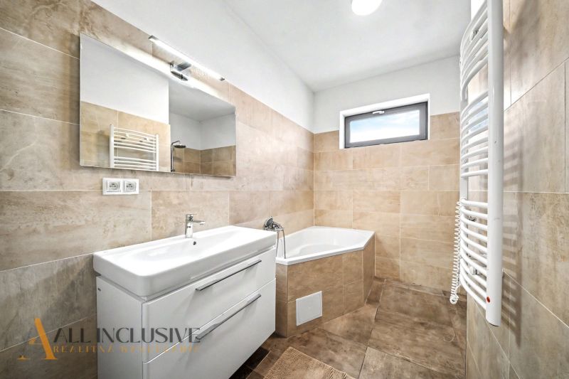 Badezimmer in einem Einfamilienhaus mit Waschbecken, Eckbadewanne und Fliesen in Beigetönen.