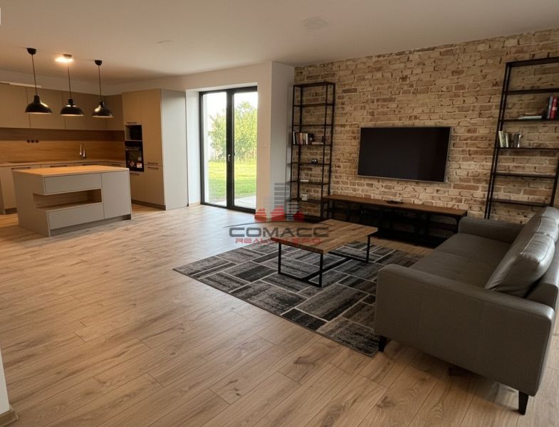 Wohnzimmer mit Küche in einem Einfamilienhaus mit Holzboden und Ziegelwand.