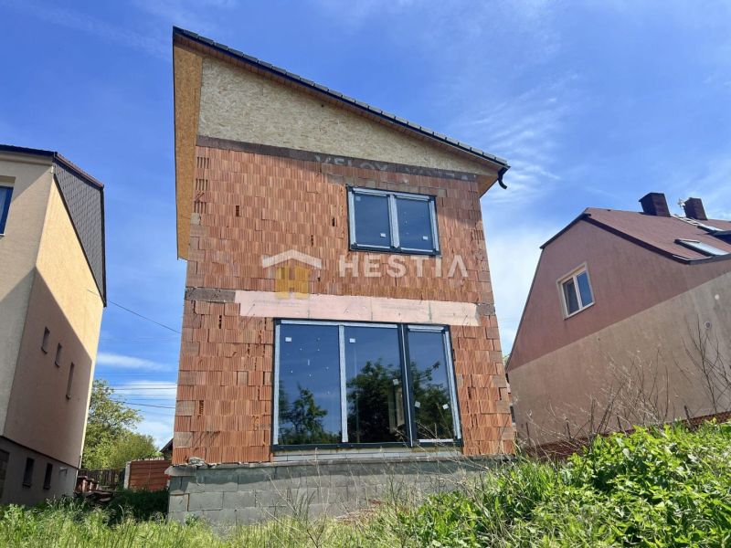 Ein Einfamilienhaus in Cerová mit unvollendeter Ziegelfassade und großen verglasten Türen.