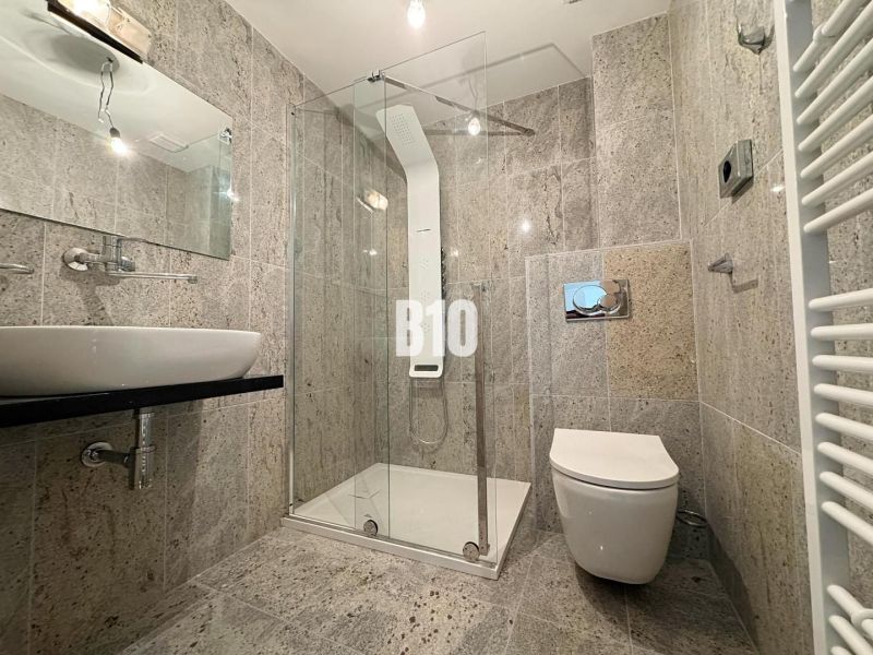 Badezimmer in einer 2-Zimmer-Wohnung mit Steinverkleidung, Duschkabine und Spiegel.