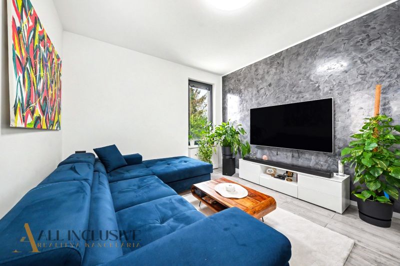 Wohnzimmer in einer 3-Zimmer-Wohnung mit ausziehbarem Sofa, Fernseher und Pflanzen.