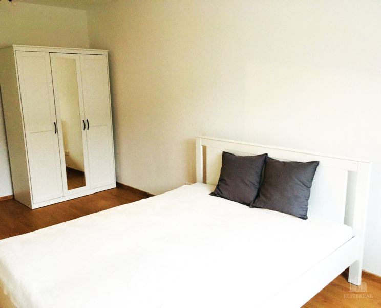 Schlafzimmer in einer 2-Zimmer-Wohnung mit einem weißen Bett und einem Kleiderschrank auf Holzboden.