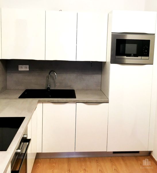 Weiße Küche mit Mikrowelle und eingebautem Spülbecken, 2-Zimmer-Wohnung, Boden mit Holzdekor.