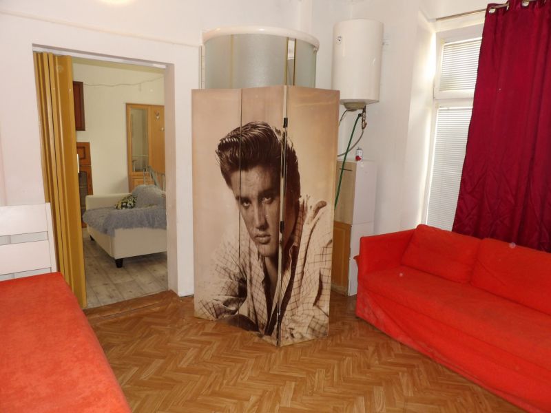 Ein rotes Sofa und ein Paravent mit einem schwarz-weißen Foto in einer 2-Zimmer-Wohnung mit bunten Vorhängen.