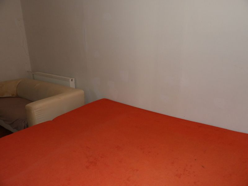 Ein Zimmer mit einem orangefarbenen Bett und einem beigen Sessel in einer Zweizimmerwohnung.