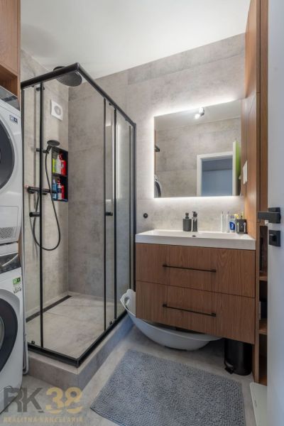 Badezimmer mit Waschmaschine, Duschkabine, Waschbecken und Möbeln mit Holzdekor in einer 2-Zimmer-Wohnung.