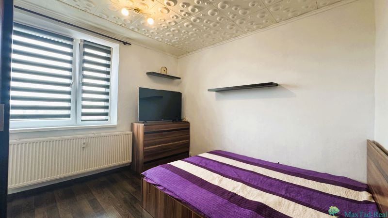 Schlafzimmer in einer 4-Zimmer-Wohnung mit Bett, Fernseher, Holzboden und modernen Jalousien.