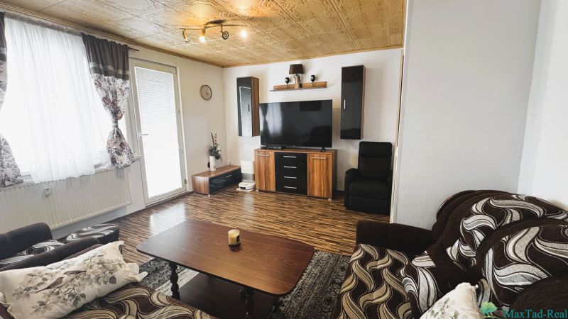 Wohnzimmer in einer 4-Zimmer-Wohnung mit Holzboden und einem Fernseher an der Wand.