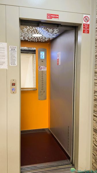 Ein offener Aufzug in einem Gebäude mit einer 4-Zimmer-Wohnung mit orangem Interieur.