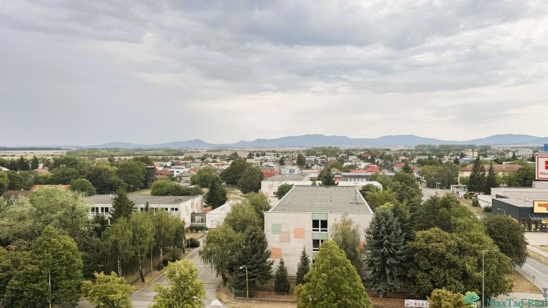 Blick auf die Komenského-Straße in Trebišov mit Gebäuden und Grünflächen.