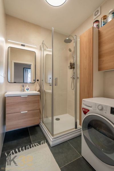 Badezimmer in einer 3-Zimmer-Wohnung mit Waschmaschine, Dusche und Waschbecken mit Stauraum.