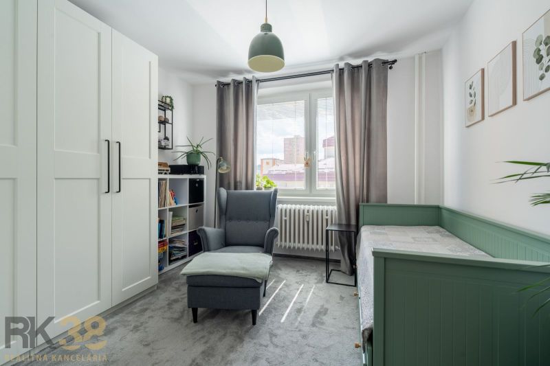 Helles Zimmer mit Sessel, Bett, Kleiderschrank und Dekorationen in einer 3-Zimmer-Wohnung.