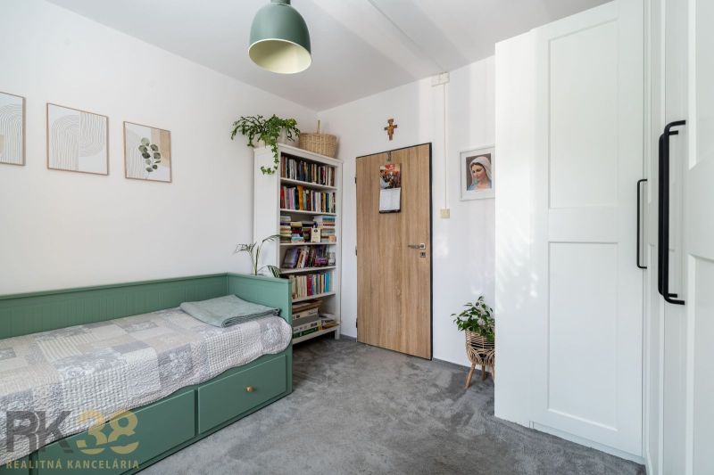 Ein Zimmer in einer 3-Zimmer-Wohnung mit einem Bett, Büchern, Pflanzen und einer Lampe.