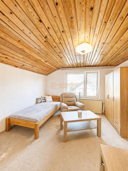 Innenraum eines Einfamilienhauses mit Holzdecke, Sessel und Bett neben dem Fenster.