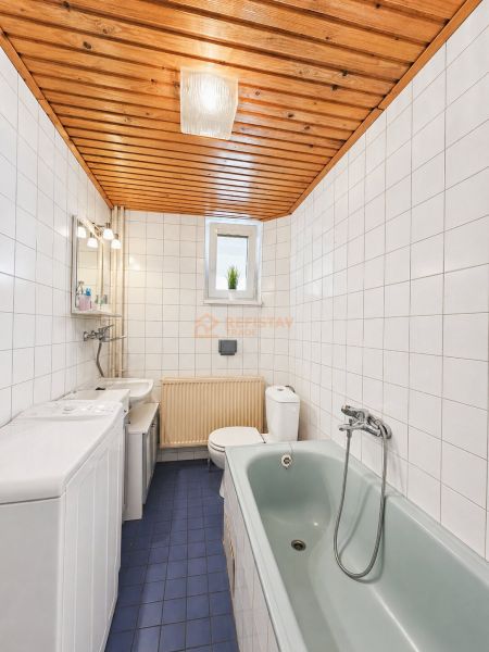 Badezimmer mit Fliesen, blauem Boden, Badewanne und Holzdecke in einem Einfamilienhaus.