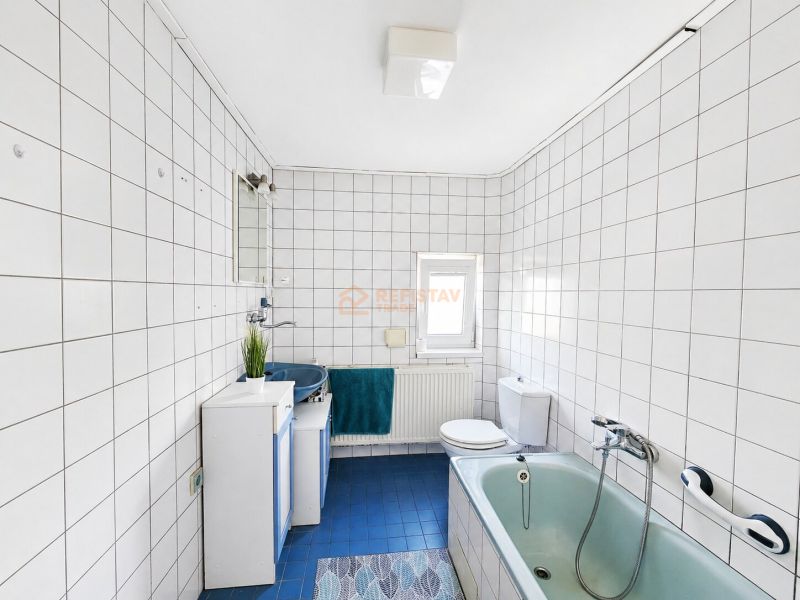Ein Badezimmer mit Dusche und Badewanne, gefliest mit weißen Fliesen, in einem Einfamilienhaus.