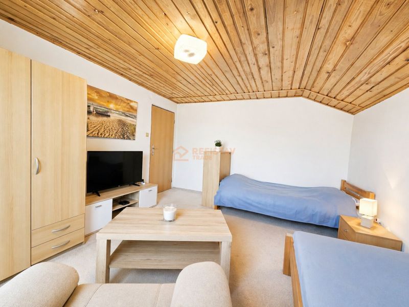 Izba v rodinnom dome s dreveným stropom, posteľami a TV.  
Zimmer in einem Einfamilienhaus mit Holzbalkendecke, Betten und Fernseher.