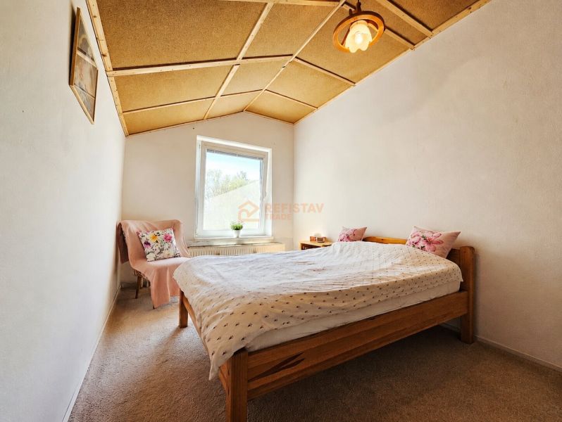 Schlafzimmer in einem Einfamilienhaus mit Holzdecke, Teppich und Bett mit Kissen.