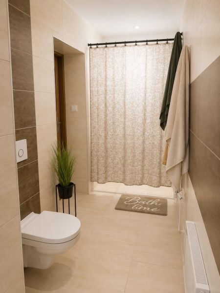 Badezimmer im Einfamilienhaus mit Toilette, Duschvorhang und heller Fliesenverkleidung.