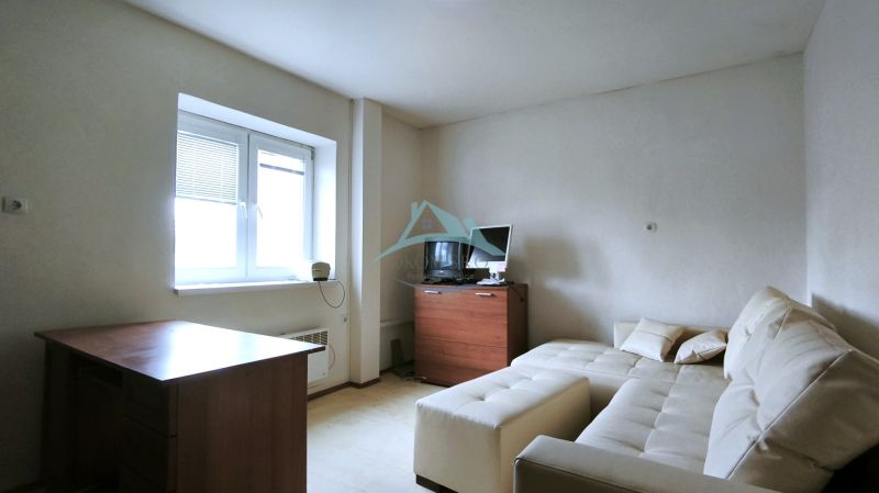 Ein Zimmer mit Sofa, Tisch, Holzelementen, Fernseher und Fenster mit Rollläden.