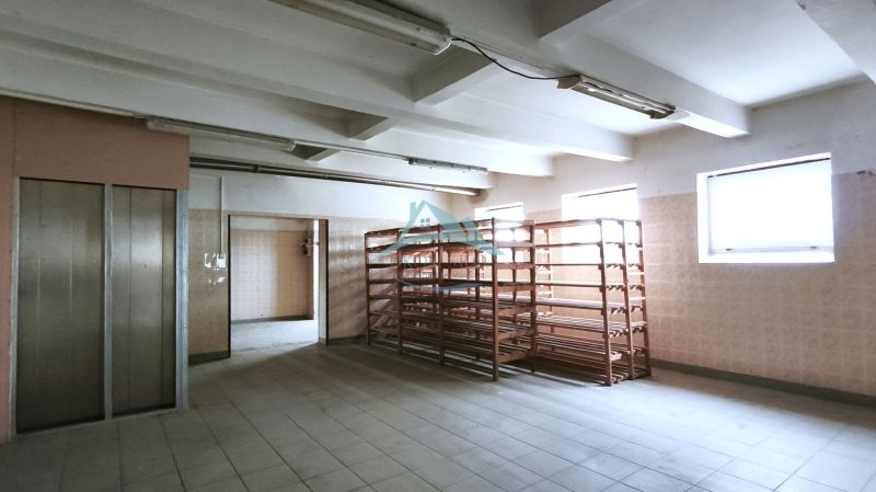 Produktionsräume mit Regalen und Aufzug, beleuchtet durch Fenster, mit Keramikboden.
