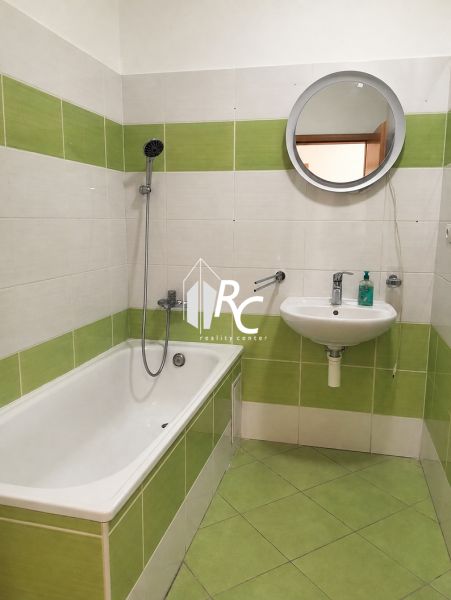 Badezimmer in einer Zweizimmerwohnung mit smaragdgrünen Fliesen und einem runden Spiegel.