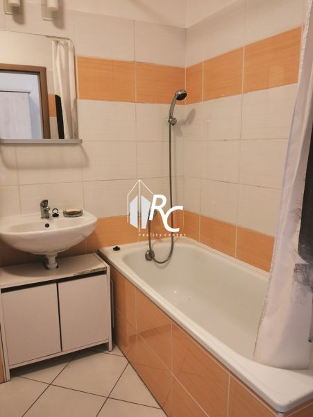 Ein Badezimmer in einer 2-Zimmer-Wohnung mit einer Badewanne und orange-weißen Fliesen.
