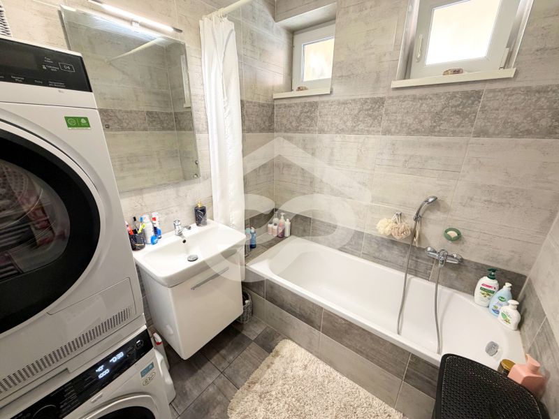 Badezimmer in einem Einfamilienhaus mit Badewanne, Waschbecken und Waschmaschine mit Trockner.