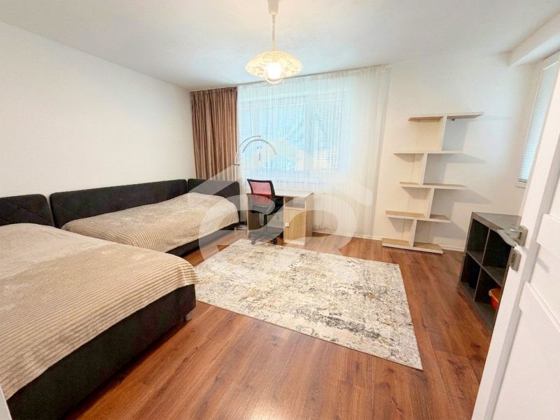 Zwei Betten, ein Schreibtisch und ein Regal in einem Zimmer eines Einfamilienhauses mit einem Boden in Holzoptik.
